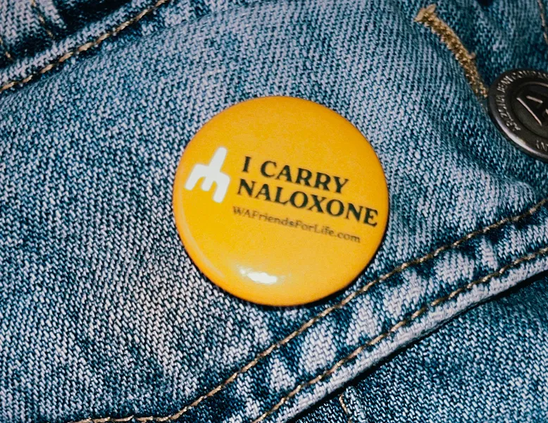 close up of "I Carry Naloxone" button on pants.