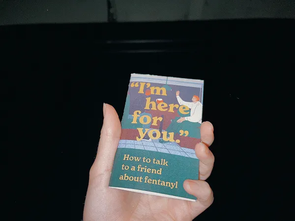 Image of a person's hand holding a small pamphlet with a dark background and the text, I'm here for you.