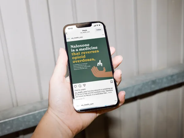 Image of a phone on a dark background with a hand holding naloxone
