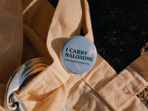 Image of a metal button that says I carry Naloxone