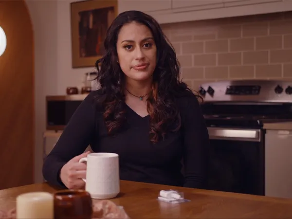 A female sitting at a table, with a cup in her hand.